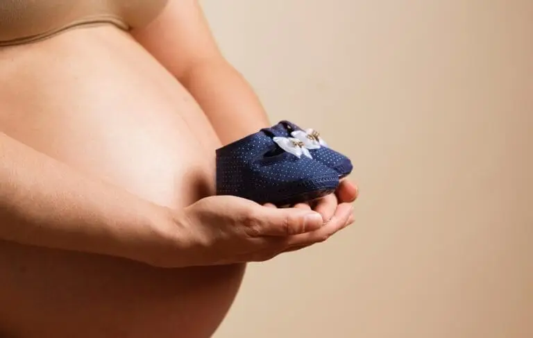 Close-up of a pregnant woman holding baby shoes, symbolizing anticipation and motherhood indoors.